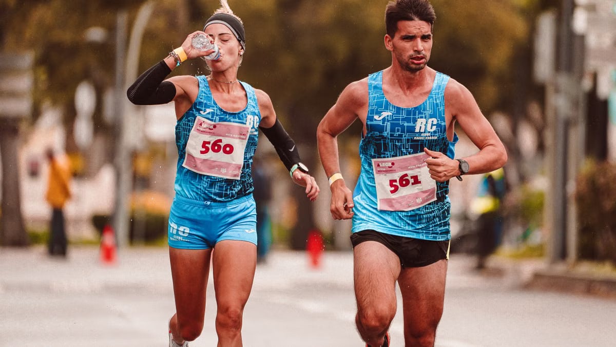Two athletes participating in a marathon, hydrating and focused, while running outdoors on a city street.