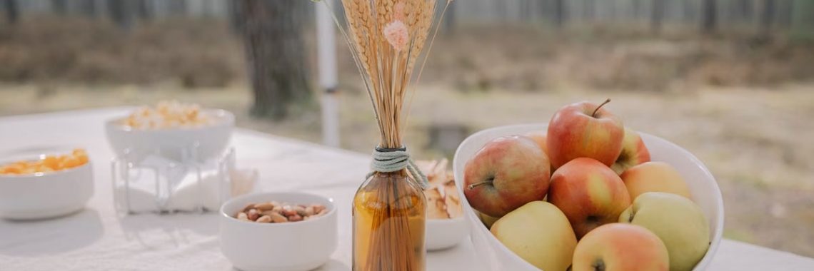 Rustic outdoor table setup featuring apples, nuts, and dried flowers in a vase, creating a cozy autumn vibe.