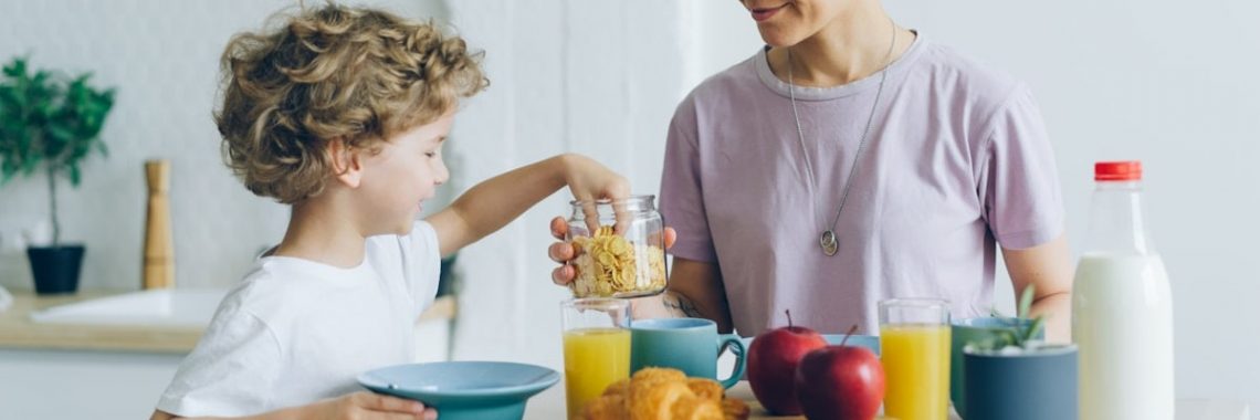Happy family mother and son eating cereal with milk at home talking