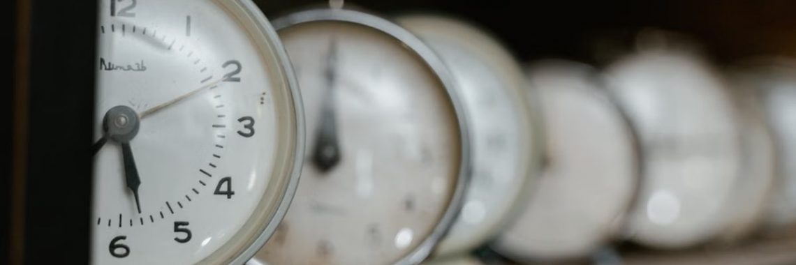 A collection of vintage analog alarm clocks displayed on a wooden shelf with blurred background.